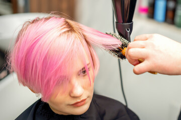 Naklejka premium Hairdresser dries pink hair of the young woman in a beauty salon