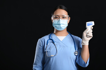 Portrait of female Asian doctor with infrared thermometer on dark background