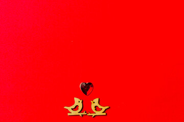 Two wooden birds in love sitting on a branch and hearts on a red background. Copy space. Valentine's day and wedding.