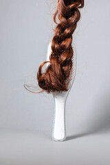 The concept of hair problems and hair care. A white comb with a false braid of hair attached to it. White background. Copy space