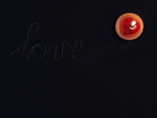 the inscription love inlaid with a silver chain on a black background and a candle flame