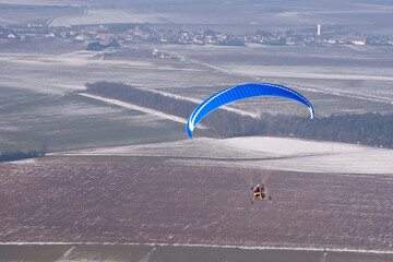 Motor paraglider flying in winter in a snow-white landscape seen from the sky