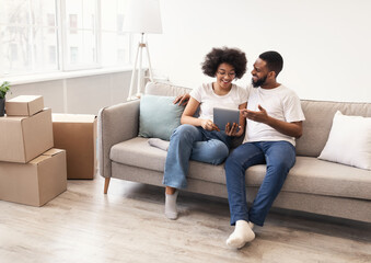 Happy Black Spouses Using Tablet Sitting Among Moving Boxes Indoor