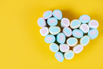Obraz premium Multicolored sweet soft marshmallow in the shape of a heart on a yellow background. Valentines day card