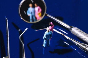 Creative concept for Dental Center and Dentist. Two miniatures of Wife and Husband look at each other on the Dental Mirror which reflects their faces towards the audience. dental treatment,teeth shiny