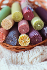 Fototapeta na wymiar Set of colored decorative natural beewax candles with a honey aroma for interior in a basket on a white knitted sweater. Selective focus. A delicate color palette. Close up