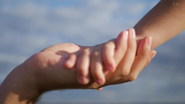 Parent holds the hand of a small child, hand of kid or child and parent or mother show love relationship teamwork together. Lovely couple holding hands on blue sky.