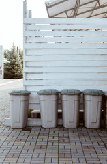 Four closed plastic garbage rubbish bins at backyard outdoors near white wooden wall 