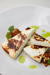 Homemade grilled feta cheese with Greek greens. Chunks of grilled cheese close-up on a plate.