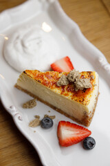 Cake with cream and strawberries on a dark wood background. A piece of cake close-up on a plate.
