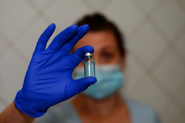 one woman wearing a medical mask and blue medical gloves holds a vial of vaccine in front of her face