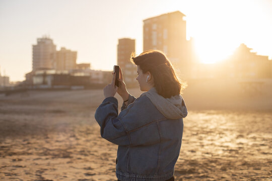 girl takes photos on phone of  sunset on beach of the Atlantic ocean