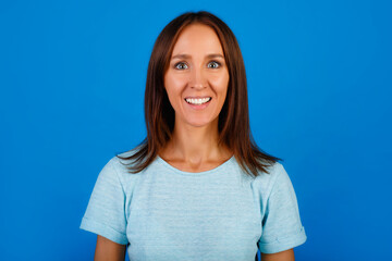 Fototapeta premium Portrait of a smiling brunette in a blue t-shirt looking at the camera, isolated on a blue background.