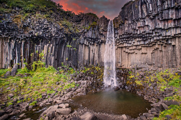 Iceland. Dramatic waterfall surrounded by dark basalt lava hexagonal columns