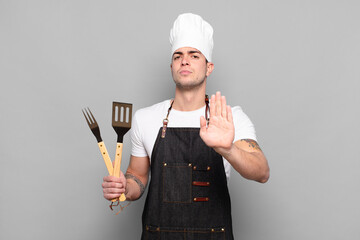young man looking serious, stern, displeased and angry showing open palm making stop gesture