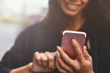 Closeup image of a beautiful mixed race woman holding, using and looking at smart phone.