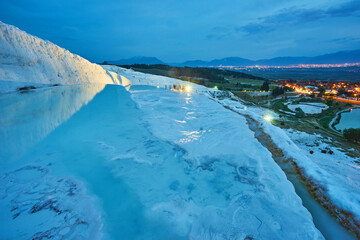 Pamukkale travertines in foreground. Sunset sky and illuminated houses