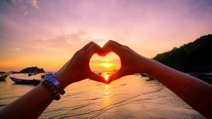 Female hands in the form of heart  in sunset sky at the sea