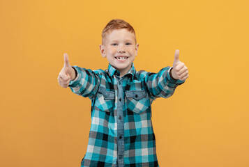 Happy ginger kid showing thumbs up on yellow studio background