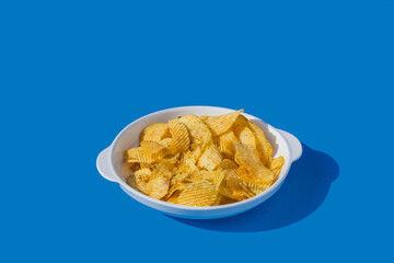 Potato chips fall into a white plate on a blue background. Flying chips.