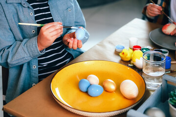 Little boy painting wooden eggs for Easter decoration