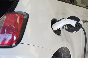 Electric car charging on parking lot with electric car charging station on city street. Close up of power supply plugged into an electric car being charged