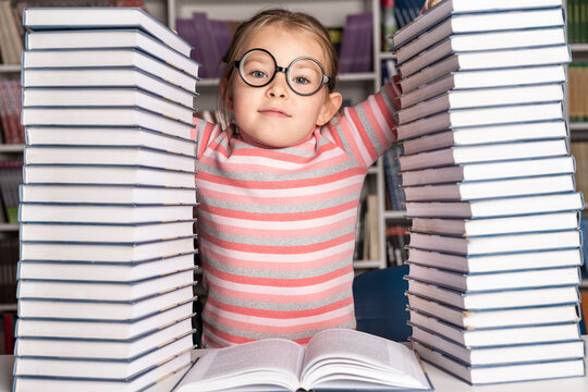 Little girl reads a book surrounded with piles of books in library. Education and Back to school concept. . High quality photo