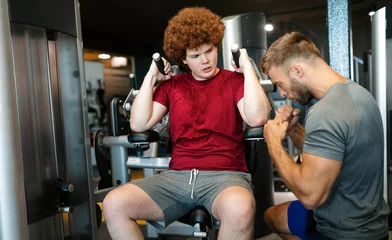 Foto op Plexiglas Overweight young man exercising gym with personal trainer © NDABCREATIVITY
