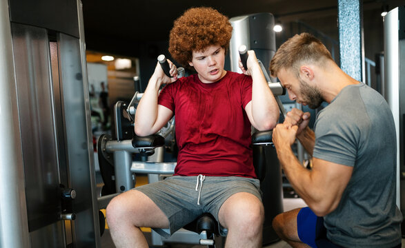 Overweight Young Man Exercising Gym With Personal Trainer