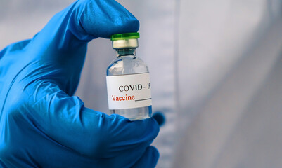 COVID-19 vaccine. Doctor wearing blue protective gloves holding an ampouled coronavirus vaccine . New Normal Lifestyle concept.