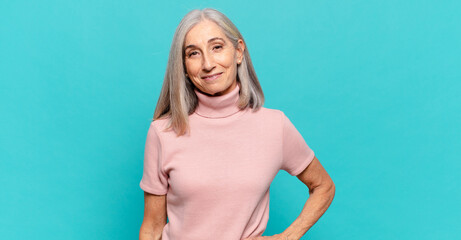 middle age woman smiling happily with a hand on hip and confident, positive, proud and friendly...