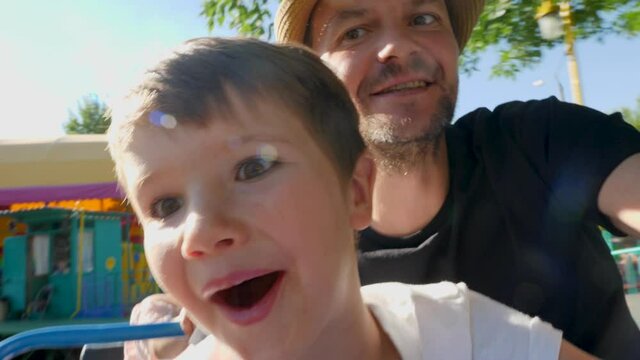 Selfie Of Father And Son Enjoying Riding Extreme Roller Coaster Attraction In Theme Park Rides Or Luna Park. Close Up Smiling Kid With Happy Dad In Amusement Park Having Fun On Rollercoaster Ride