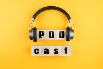 word PODCAST on wooden blocks and headphones on orange background, podcasting concept