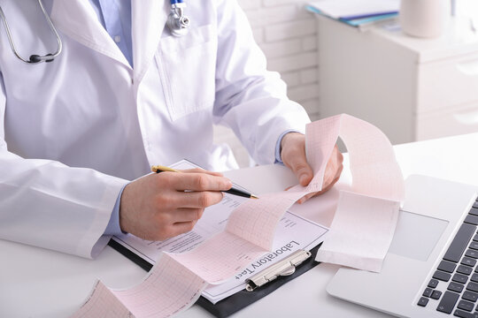 Doctor examining cardiogram at table in clinic, closeup