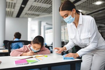 Fototapeta premium Teacher in mask cleaning table with antibacterial sanitizer and napkin