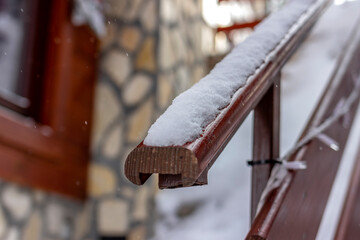 Close up of an fresh snow on the wooden handle and stairway. Wooden handle with rounded edges covered with snowflakes. Wooden handle with snow. Blurred background. Copy space.