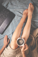 Fototapeta na wymiar Young woman drinking coffee at home in her bed and checking her phone and laptop, top view, flat lay