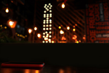 Phone on table, dark blurred cafe background. Light bokeh.