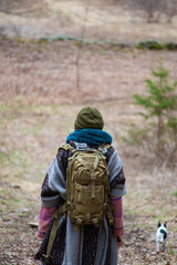 View from behind of a young woman with hippie style heavy winter clothes, wool scarf and hat looking in front of her during a walk in the woodlands.