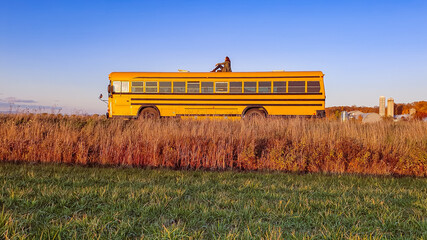 Wide angle, poetic shot of a man sitting on the top of a beautiful, bright yellow bus in the middle...