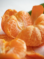 Fresh juicy bright orange tangerines with green leaves on a white cotton tablecloth in the morning light