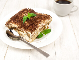 Tiramisu cake with mint leaf on a plate on a light background.
