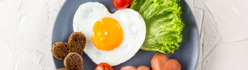 banner of Fried eggs in the shape of a heart with sausages, herbs and tomatoes. Breakfast on Valentine's day