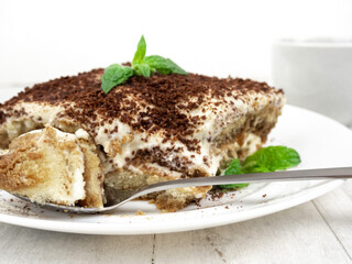 Tiramisu cake with mint leaf on a plate on a light background.