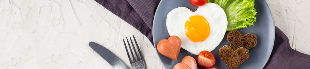 banner of Valentines day breakfast with heart shaped fried eggs served on grey plate.