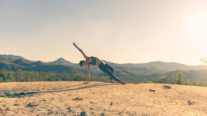 Young good looking woman perform yoga pose on mountain with sun light during sunset
