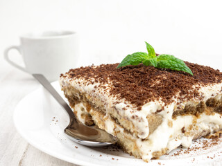 Tiramisu cake with mint leaf on a plate on a light background.