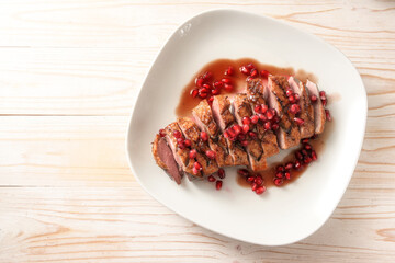 Festive roasted duck breast with pomegranate seeds and sauce on a white plate for a holiday meal,...