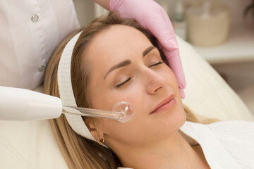 Darsonvalization of the face or rejuvenation of the face with the help of electrotherapy. Photo of darsonval for the face. Current therapy. The patient is at the beautician