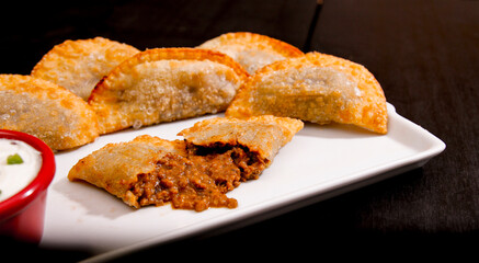 Deliciosos pasteis de carne, camarão, queijo com creme de queijo gorgonzola em recipiente branco em fundo escuro.